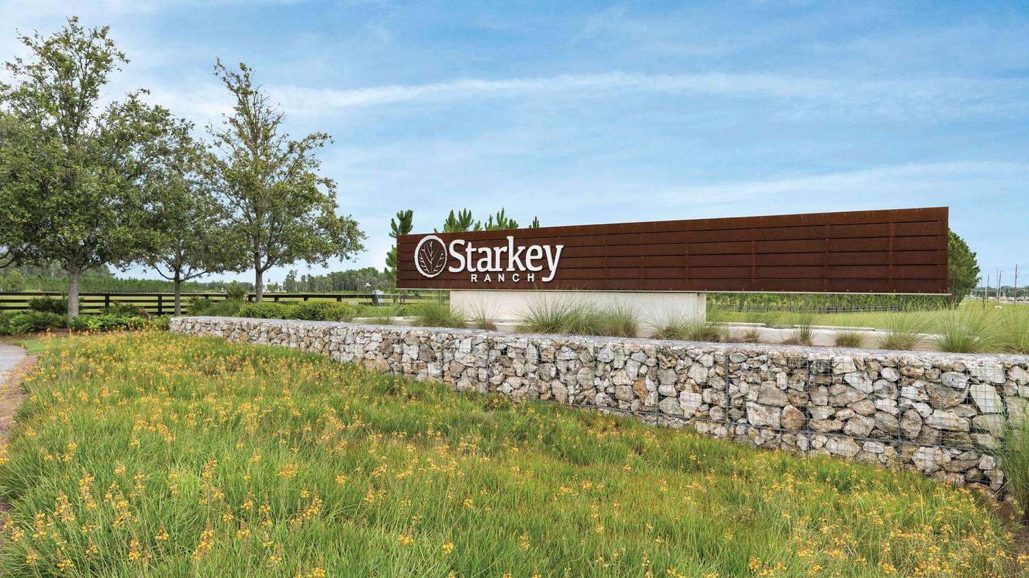 The weathered-steel Starkey Ranch entry monument above a stacked-stone wall and native wildflowers.