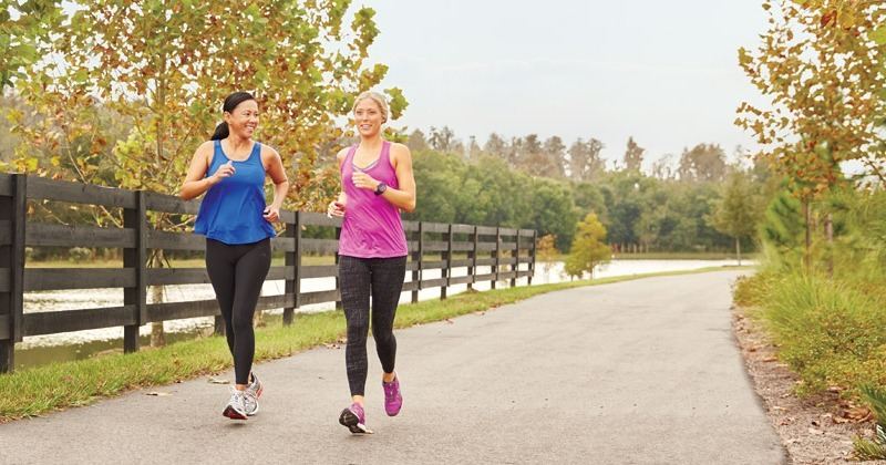 Two residents jogging along a tree-lined Starkey Ranch trail beside a ranch-rail fence.